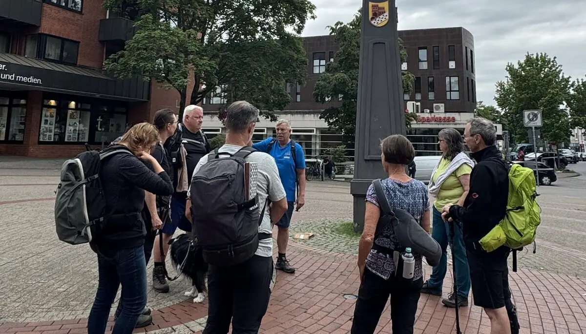 Eine Wandergruppe steht vor einer großen schwarzen Uhrsäule auf einem Platz. | © DAV Dortmund