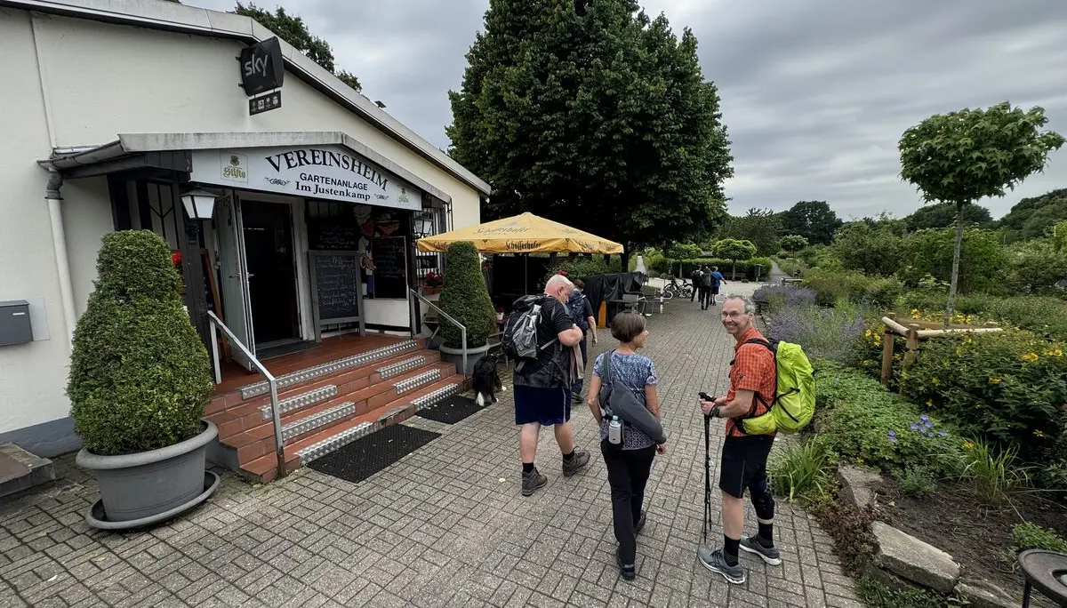 Mehrere Wandernde mit Rucksäcken stehen vor einer Gaststätte mit Biergarten. | © DAV Dortmund