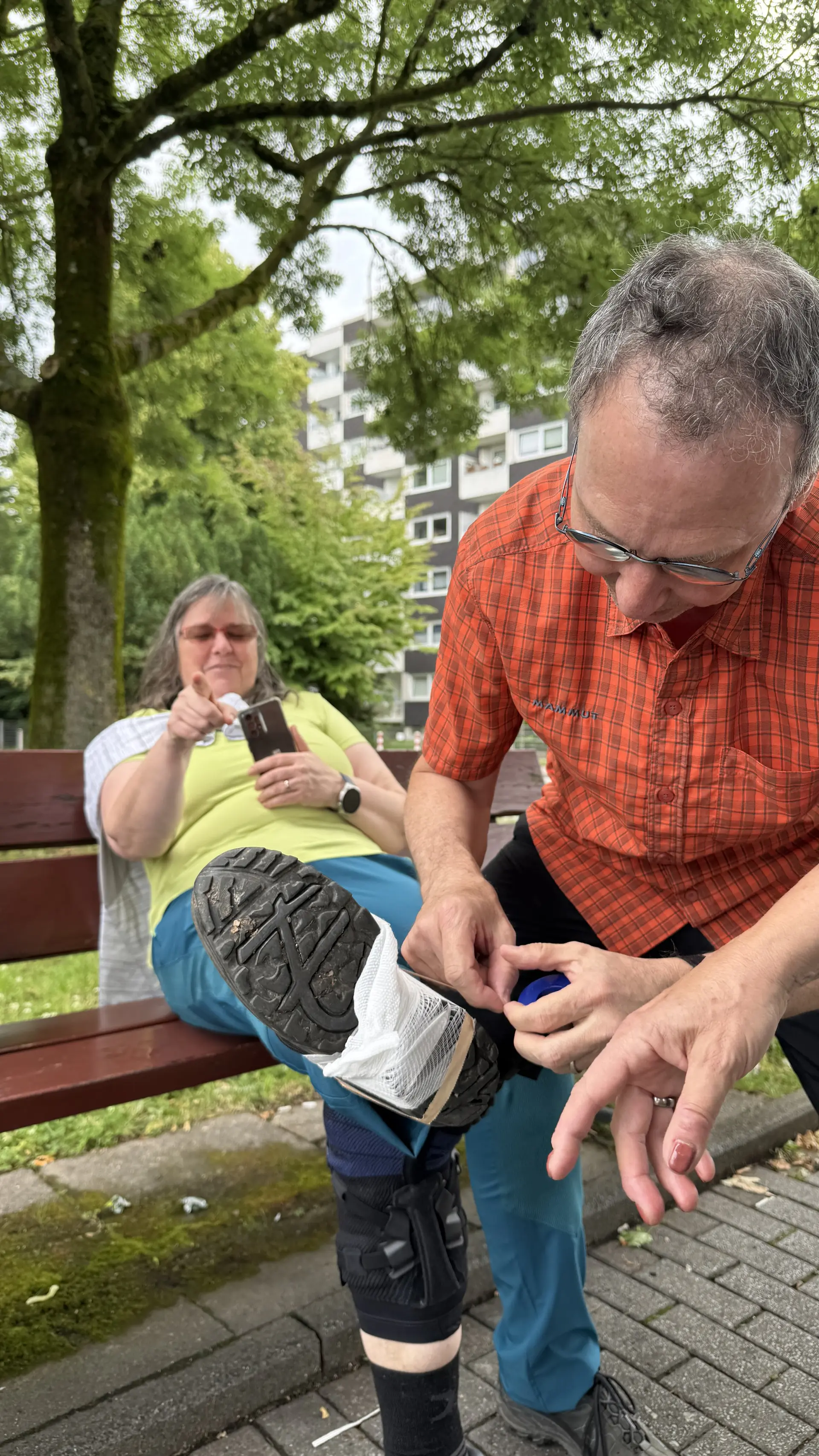 Ein Mann versorgt einen Fuß mit Verbandmaterial, eine Frau sitzt im Hintergrund auf der Bank. | © DAV Dortmund