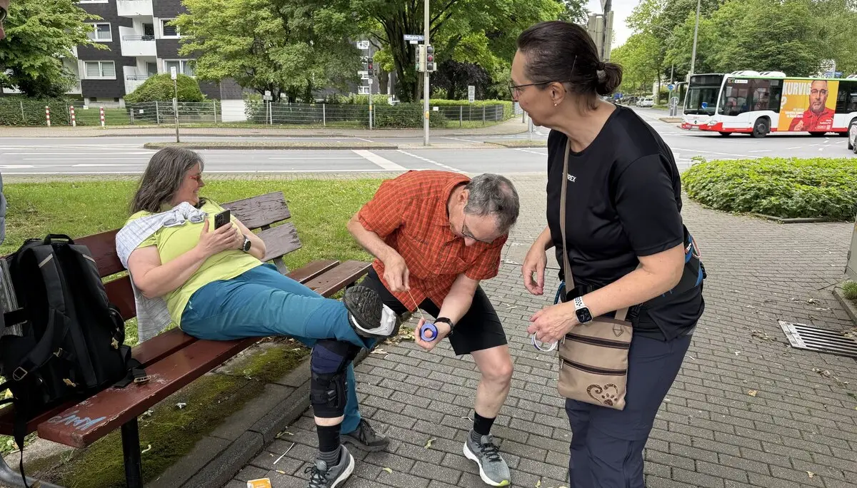 Eine Frau sitzt auf einer Bank, während ein Mann ihren Knieschutz überprüft und eine andere Frau daneben steht. | © DAV Dortmund