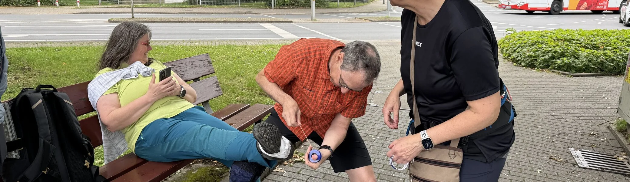 Eine Frau sitzt auf einer Bank, während ein Mann ihren Knieschutz überprüft und eine andere Frau daneben steht. | © DAV Dortmund