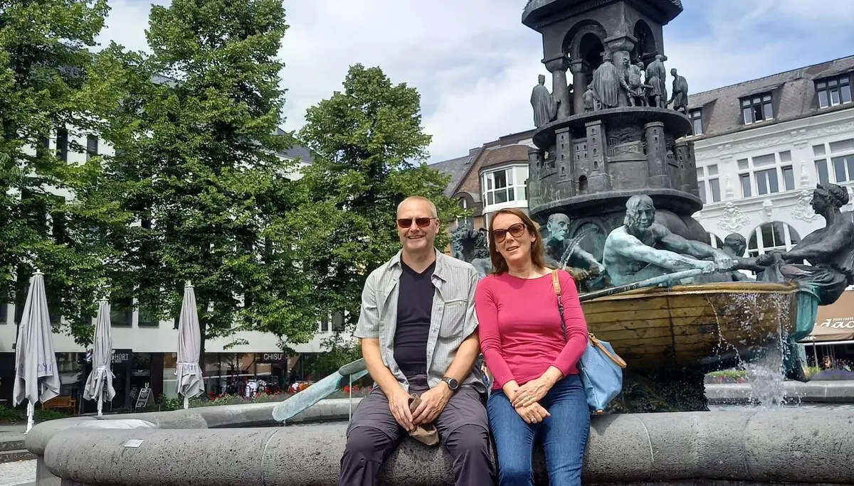 Zwei Personen sitzen auf dem Rand eines Brunnens mit kunstvoller Statue auf einem Stadtplatz. | © DAV Dortmund