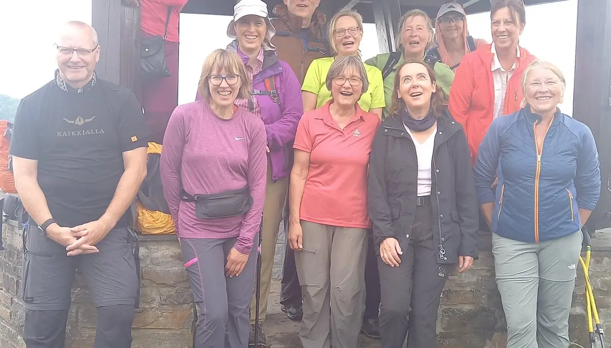 Eine Wandergruppe mit zwölf Personen steht lachend vor einem hölzernen Aussichtsturm. | © DAV Dortmund