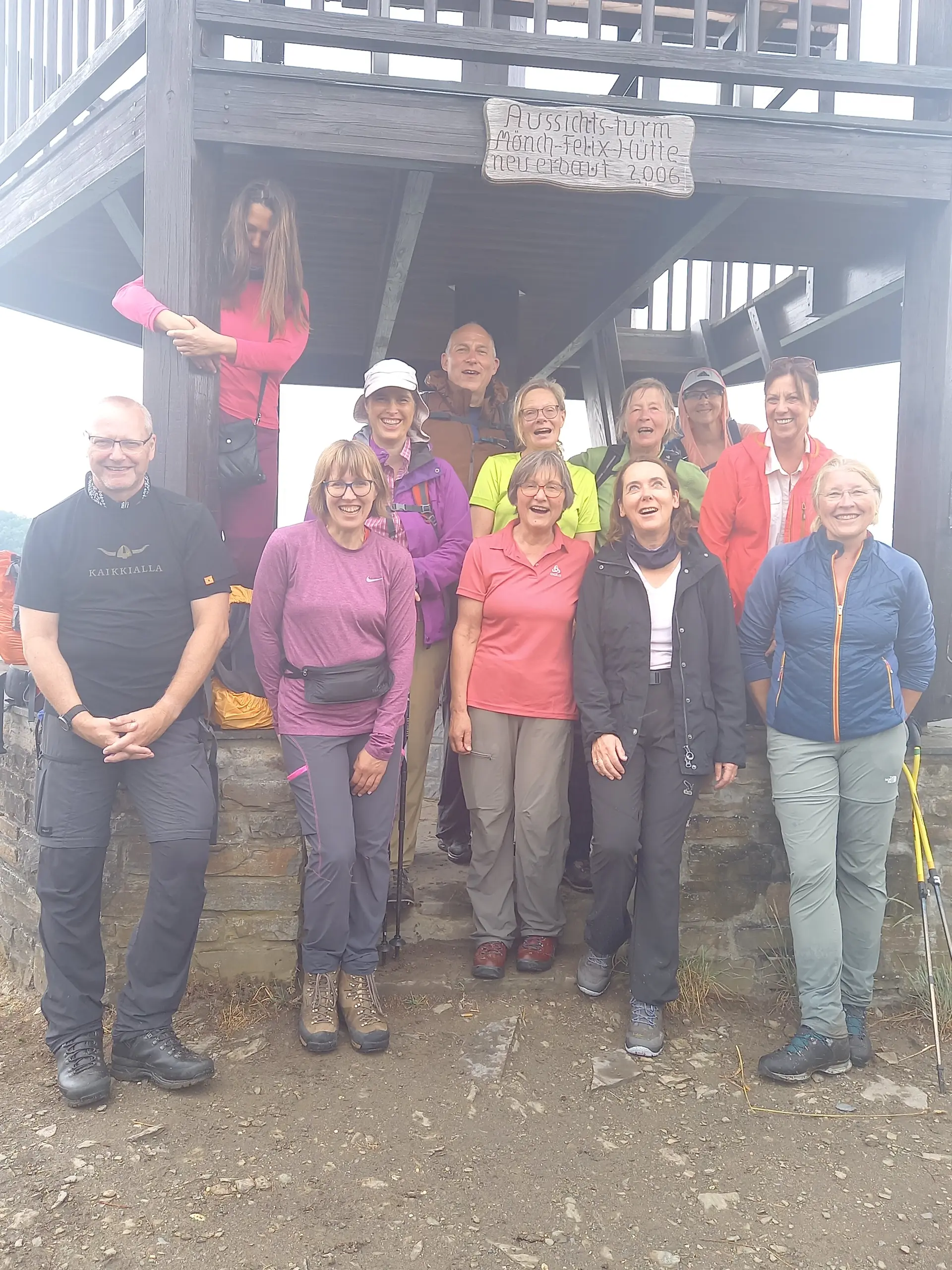Eine Wandergruppe mit zwölf Personen steht lachend vor einem hölzernen Aussichtsturm. | © DAV Dortmund