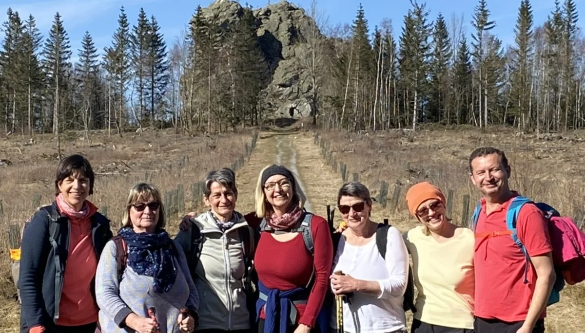 Acht Personen stehen lachend auf einer Wiese mit Felsformation und Wald im Hintergrund. | © DAV Dortmund