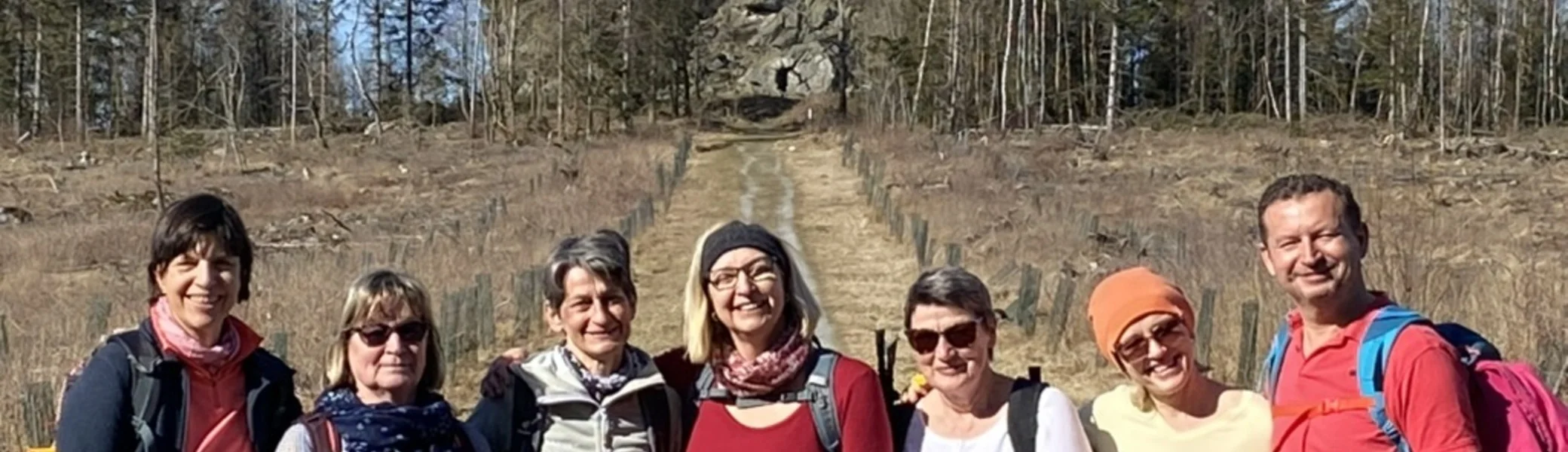 Acht Personen stehen lachend auf einer Wiese mit Felsformation und Wald im Hintergrund. | © DAV Dortmund