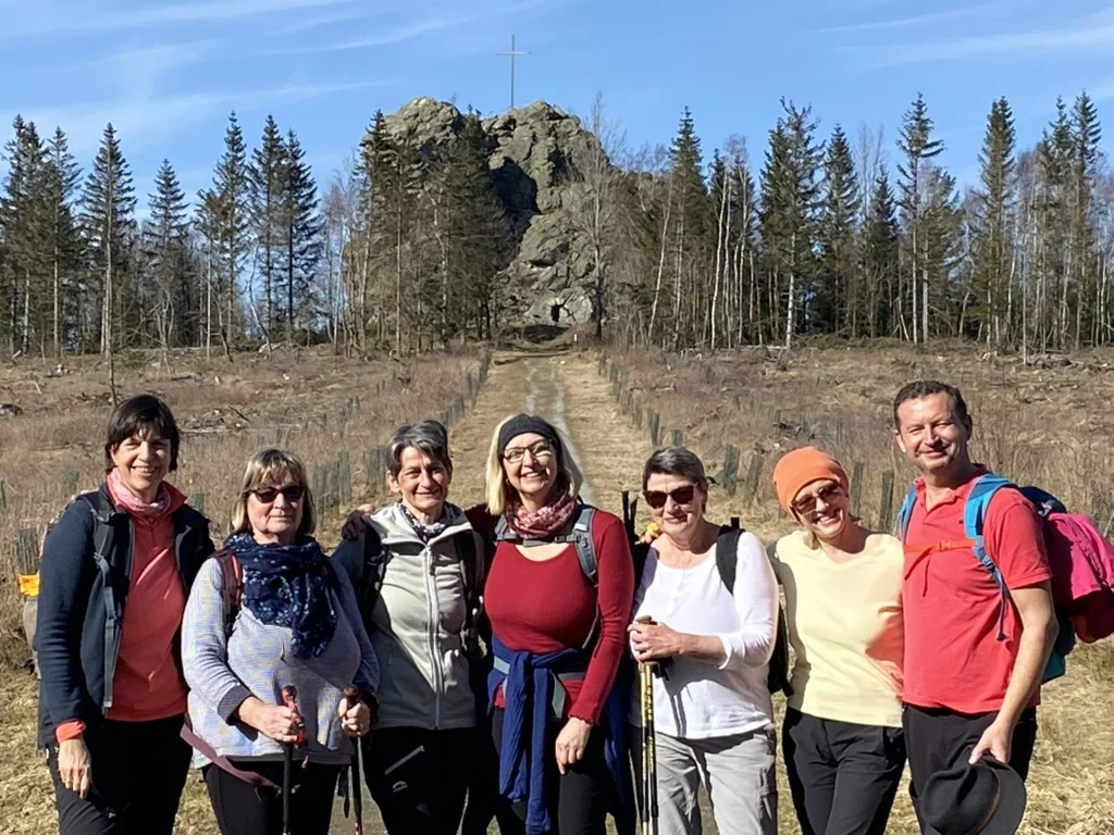 Acht Personen stehen lachend auf einer Wiese mit Felsformation und Wald im Hintergrund. | © DAV Dortmund
