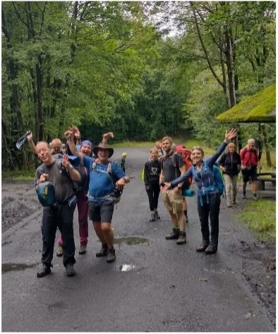 Gruppe von Wandernden posiert lachend auf einer Waldstraße | © DAV Dortmund