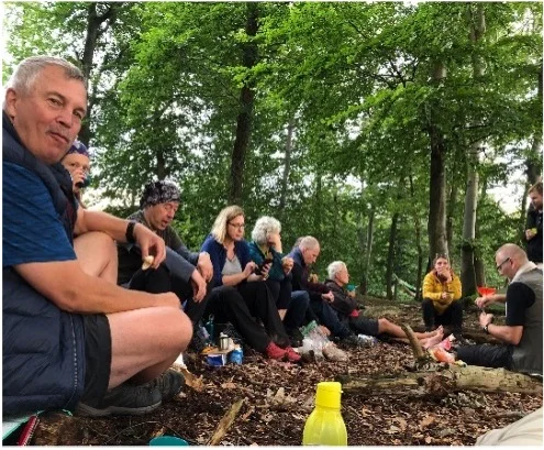 Gruppe von Wandernden macht eine Pause im Wald und sitzt auf dem Waldboden. | © DAV Dortmund