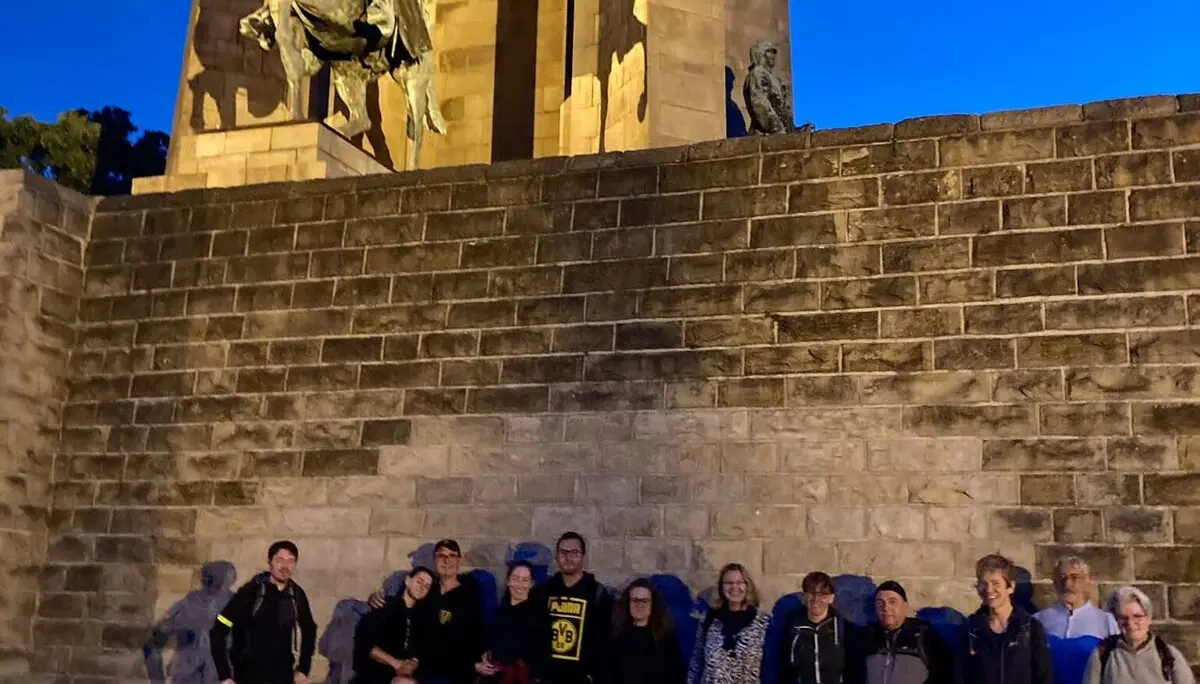 Eine Wandergruppe steht vor dem beleuchteten Reiterstandbild am Kaiser-Wilhelm-Denkmal bei Abendlicht. | © DAV Dortmund