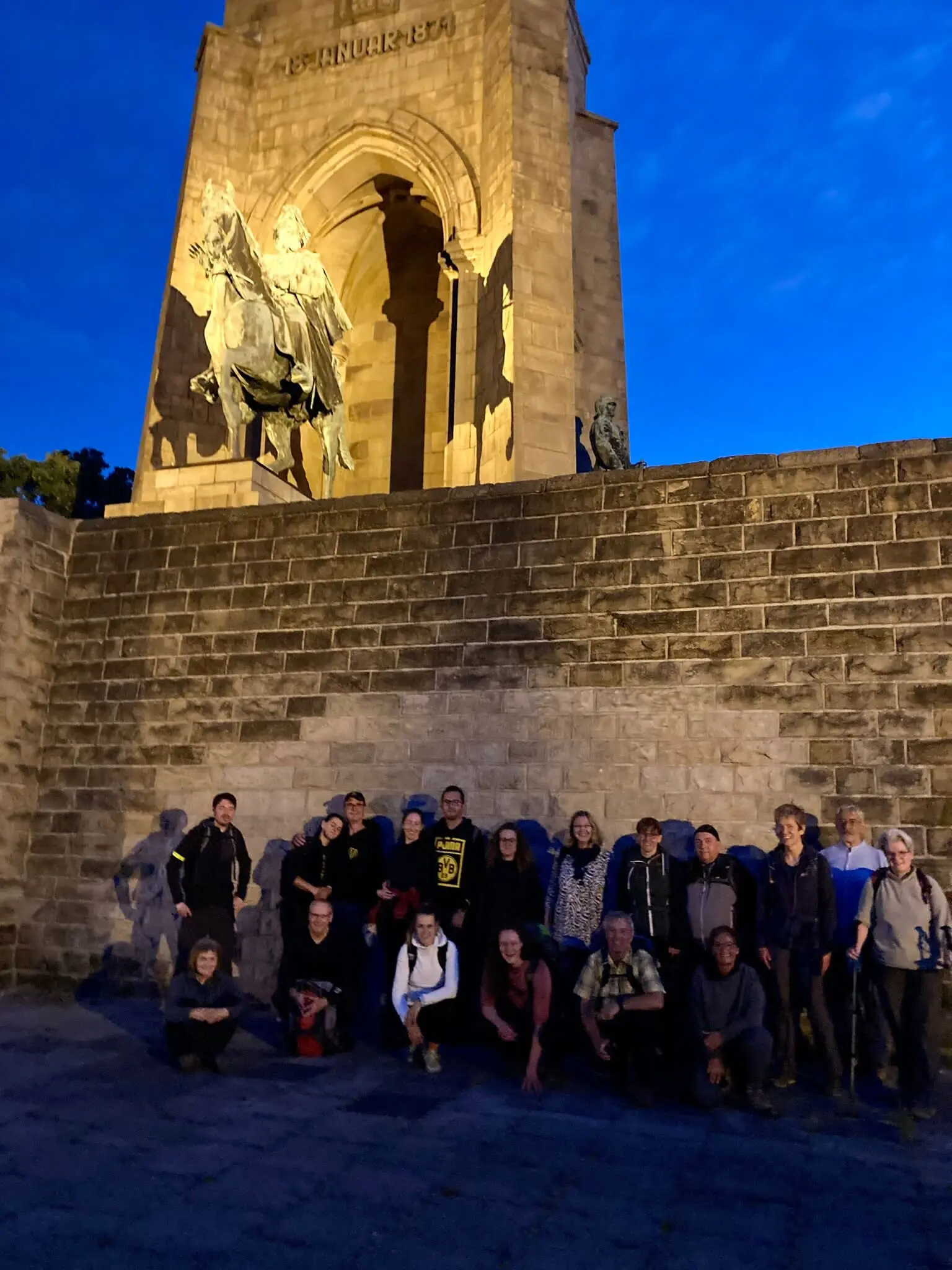 Eine Wandergruppe steht vor dem beleuchteten Reiterstandbild am Kaiser-Wilhelm-Denkmal bei Abendlicht. | © DAV Dortmund