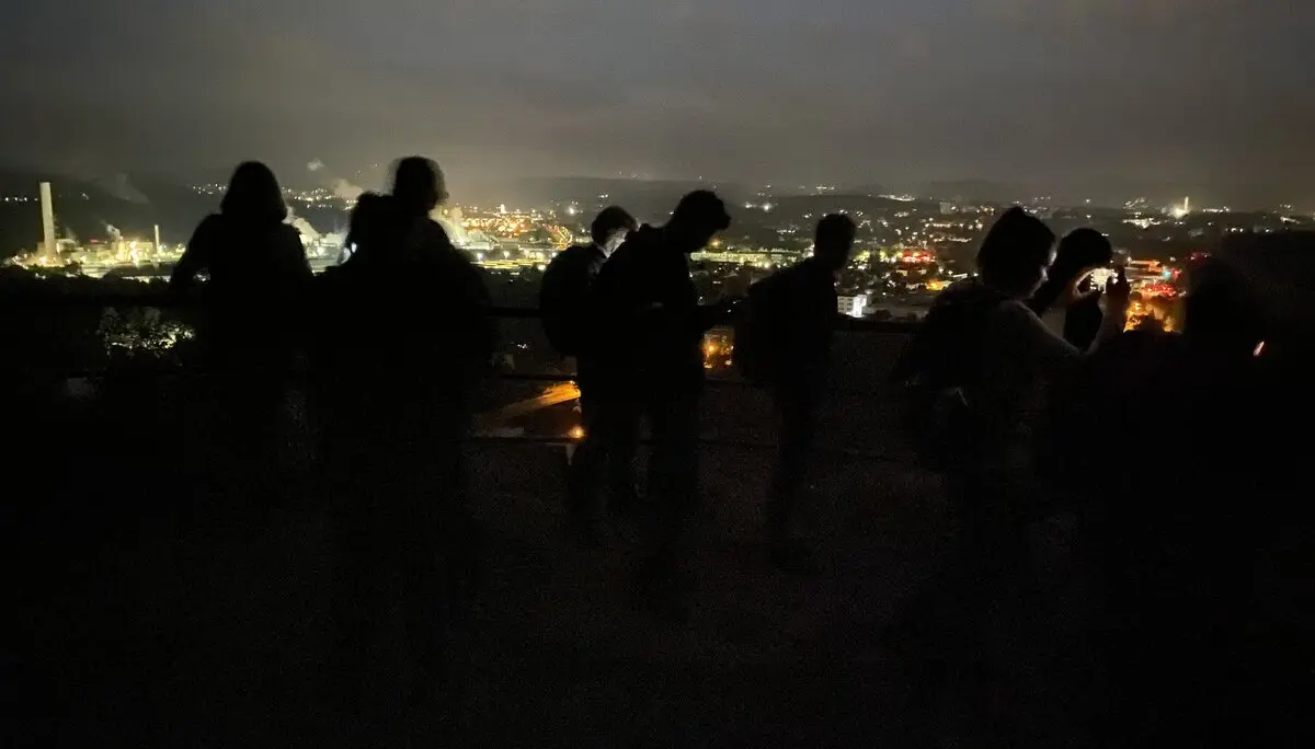 Silhouetten mehrerer Personen bei Nacht mit Blick auf eine beleuchtete Stadtlandschaft. | © DAV Dortmund