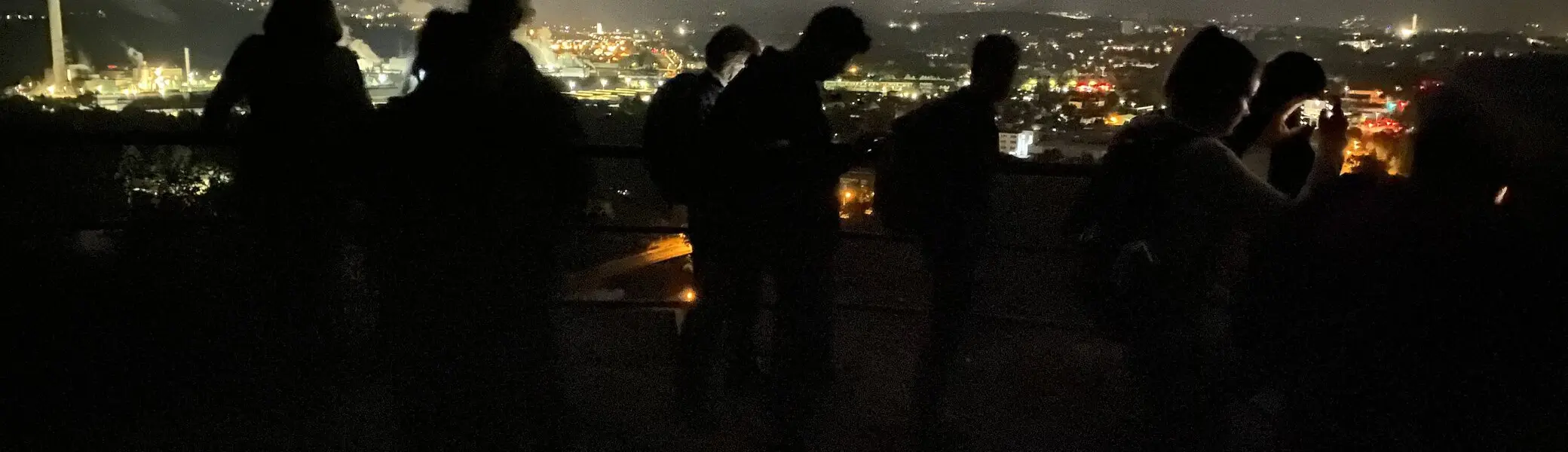 Silhouetten mehrerer Personen bei Nacht mit Blick auf eine beleuchtete Stadtlandschaft. | © DAV Dortmund