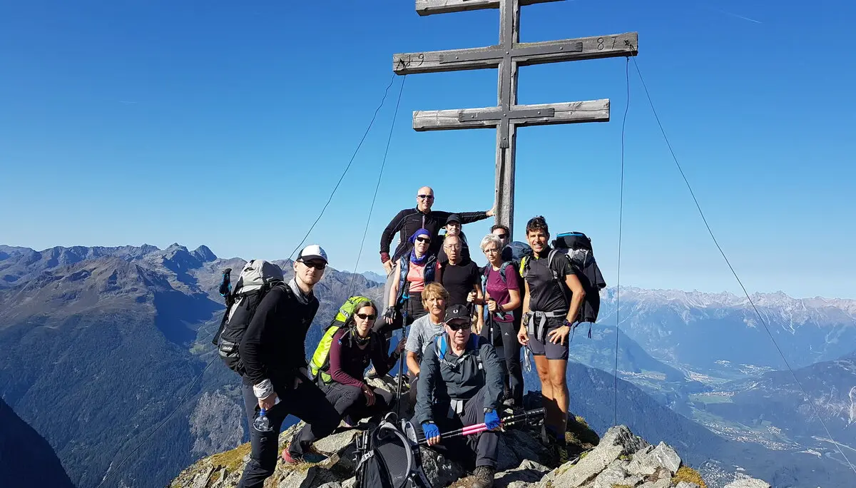 Gruppe posiert auf einem Berggipfel vor einem doppelten Holzkreuz mit weitem Ausblick. | © DAV Dortmund