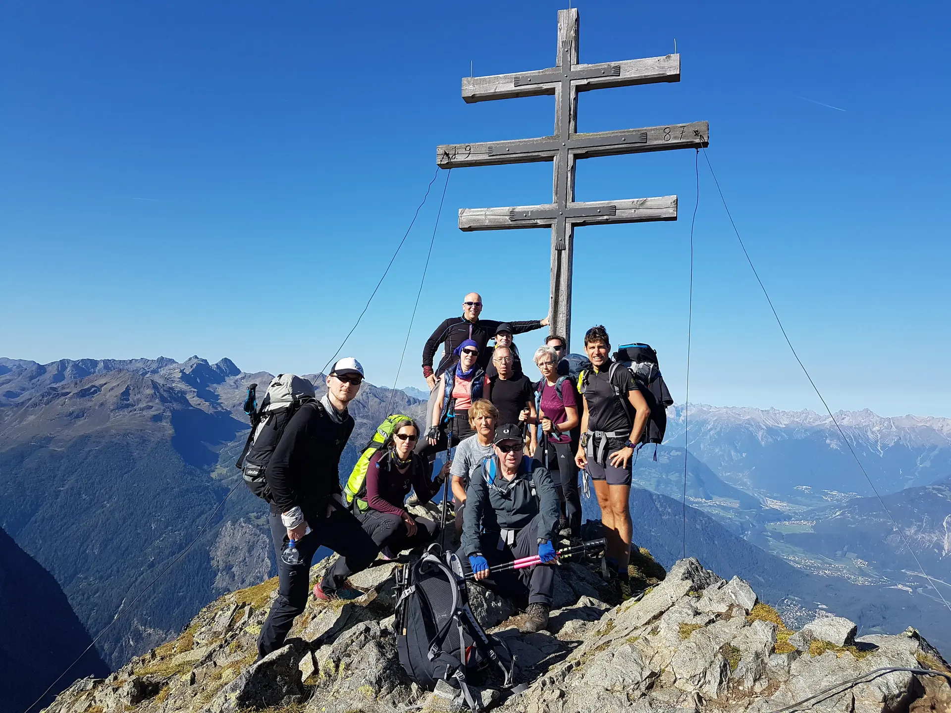 Gruppe posiert auf einem Berggipfel vor einem doppelten Holzkreuz mit weitem Ausblick. | © DAV Dortmund