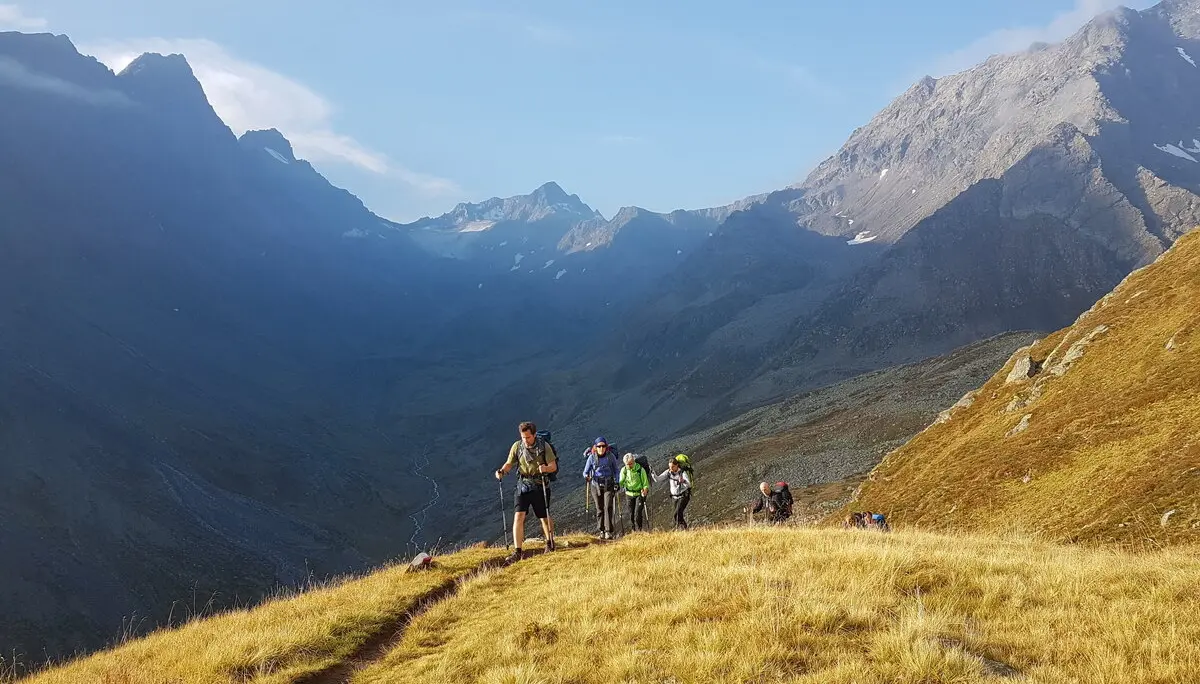 Gruppe wandert auf einem grasbewachsenen Bergrücken, umgeben von Berggipfeln bei Sonnenuntergang. | © DAV Dortmund
