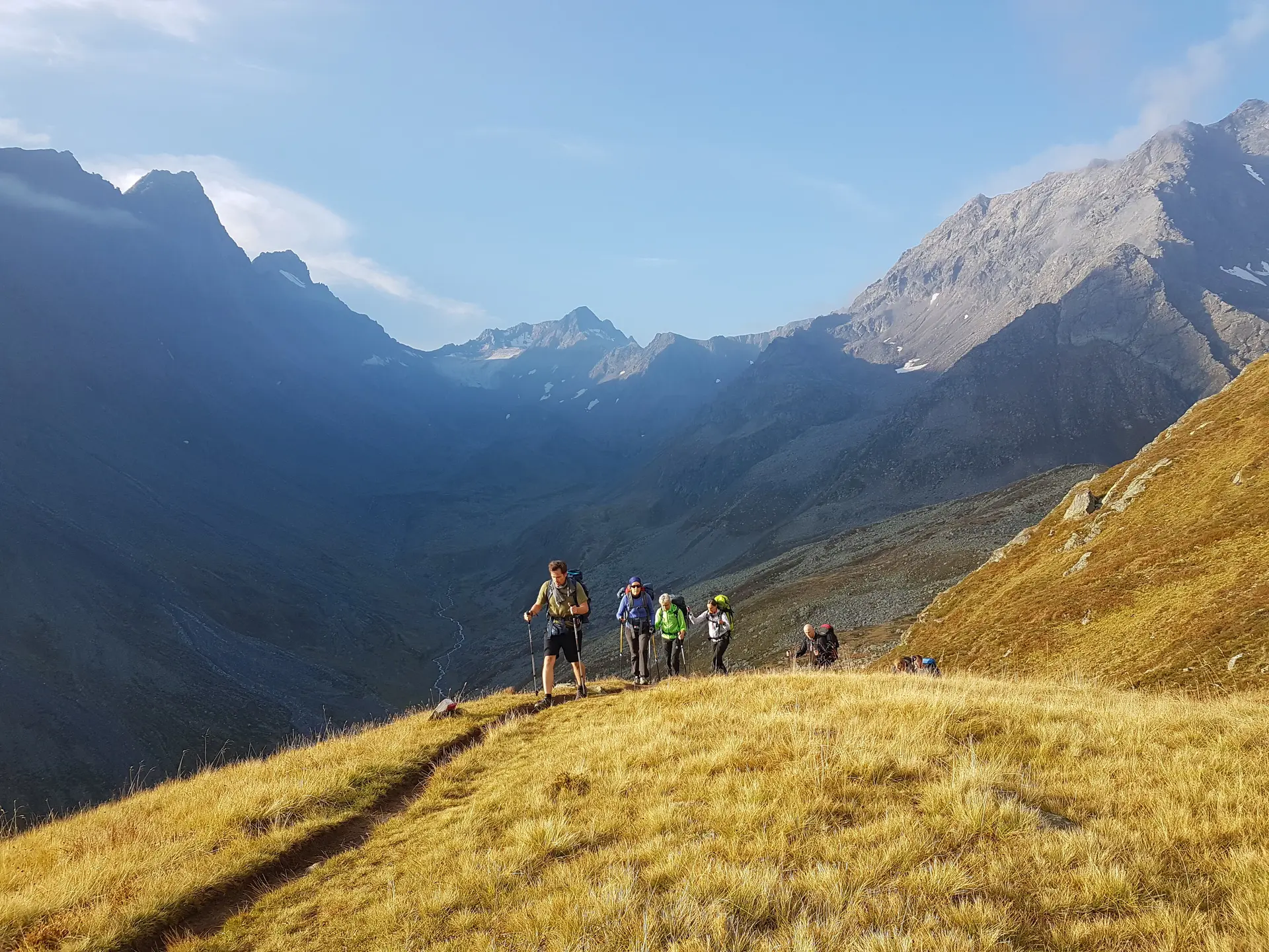Gruppe wandert auf einem grasbewachsenen Bergrücken, umgeben von Berggipfeln bei Sonnenuntergang. | © DAV Dortmund