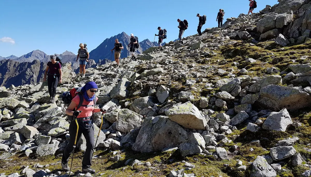 Wandergruppe steigt über felsiges Gelände bei Sonnenschein auf, Berglandschaft im Hintergrund. | © DAV Dortmund