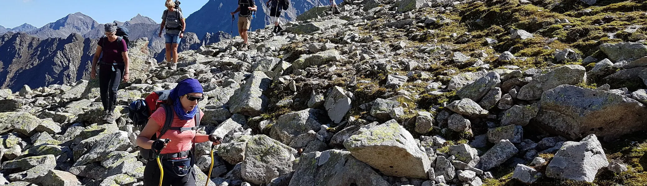 Wandergruppe steigt über felsiges Gelände bei Sonnenschein auf, Berglandschaft im Hintergrund. | © DAV Dortmund