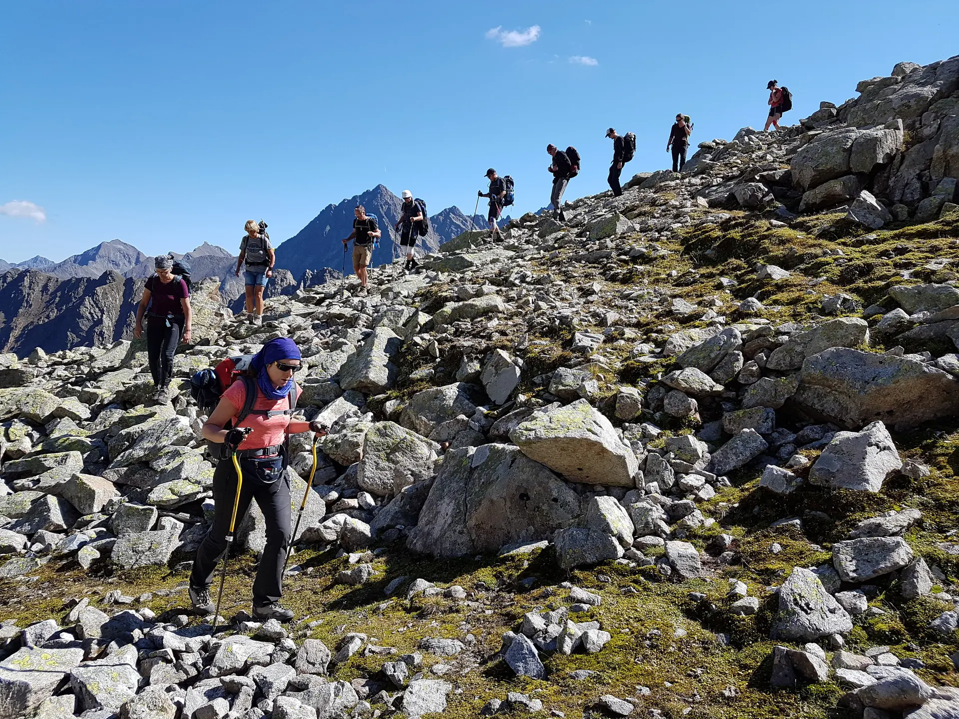 Wandergruppe steigt über felsiges Gelände bei Sonnenschein auf, Berglandschaft im Hintergrund. | © DAV Dortmund