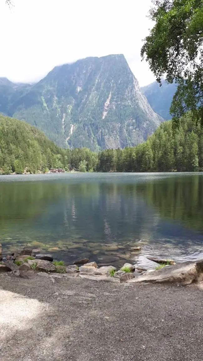 Ein ruhiger Bergsee mit Spiegelung der umliegenden Berge und Wälder, im Vordergrund ein Uferpfad. | © DAV Dortmund