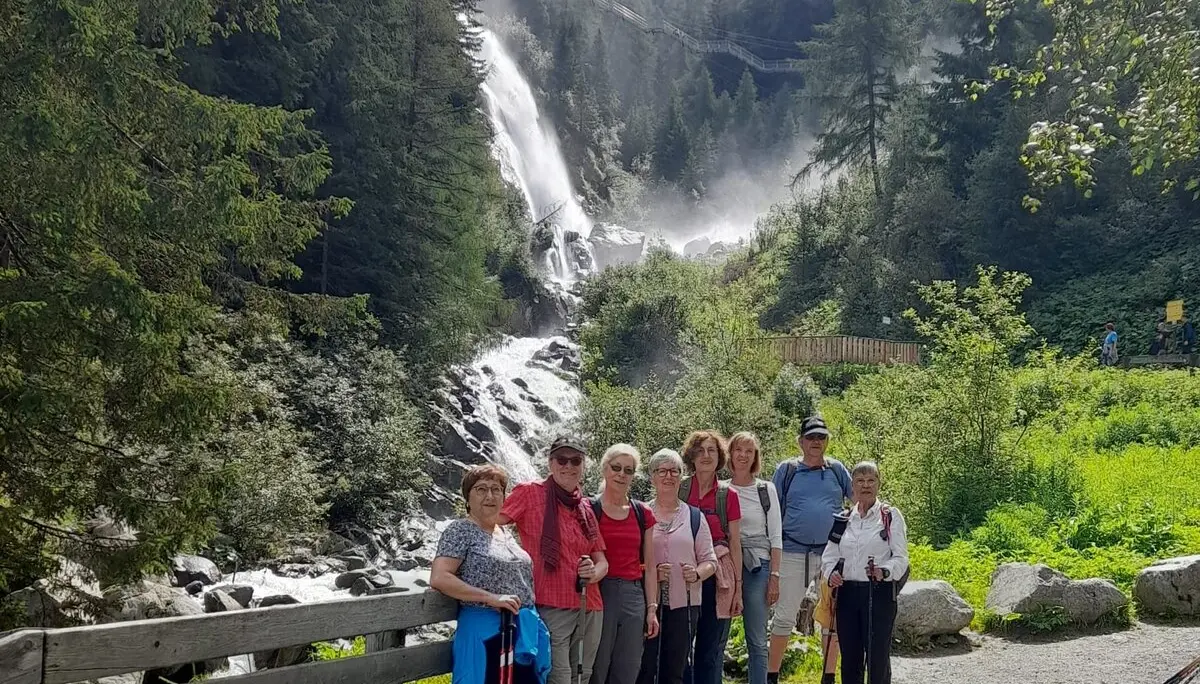 Eine Wandergruppe posiert auf einem Weg vor einem rauschenden Wasserfall in einem bewaldeten Tal. | © DAV Dortmund