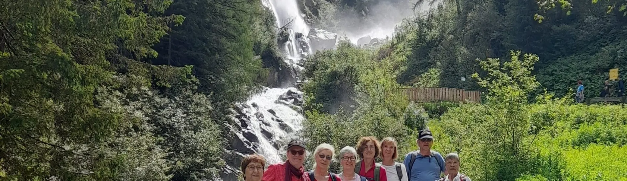 Eine Wandergruppe posiert auf einem Weg vor einem rauschenden Wasserfall in einem bewaldeten Tal. | © DAV Dortmund