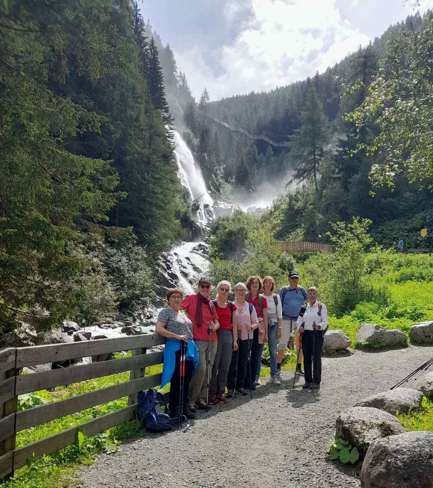 Eine Wandergruppe posiert auf einem Weg vor einem rauschenden Wasserfall in einem bewaldeten Tal. | © DAV Dortmund