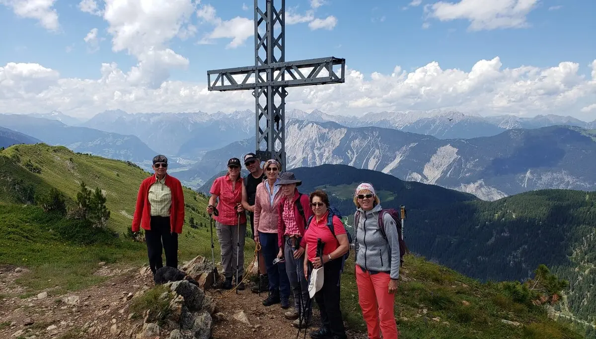 Sechs Frauen stehen am metallenen Gipfelkreuz auf einem sonnigen Berg mit Weitblick. | © DAV Dortmund