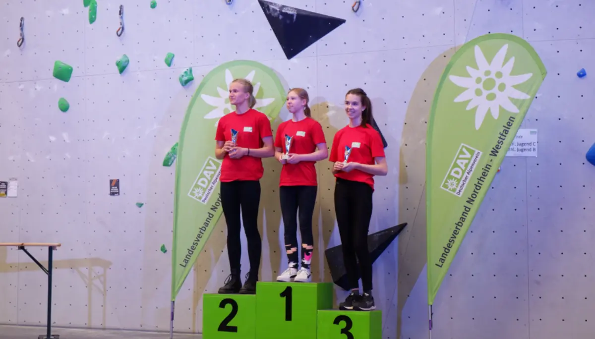 Drei Mädchen in roten Shirts stehen auf dem Siegerpodest vor DAV-Bannern. | © DAV Dortmund