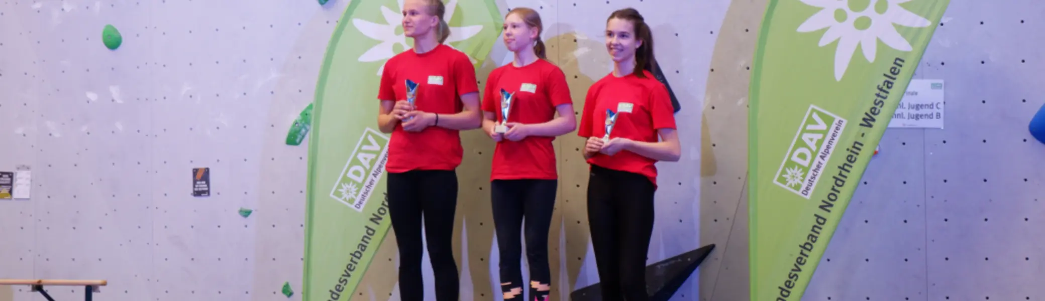 Drei Mädchen in roten Shirts stehen auf dem Siegerpodest vor DAV-Bannern. | © DAV Dortmund