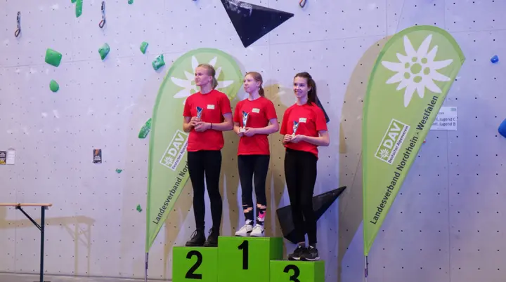 Drei Mädchen in roten Shirts stehen auf dem Siegerpodest vor DAV-Bannern. | © DAV Dortmund
