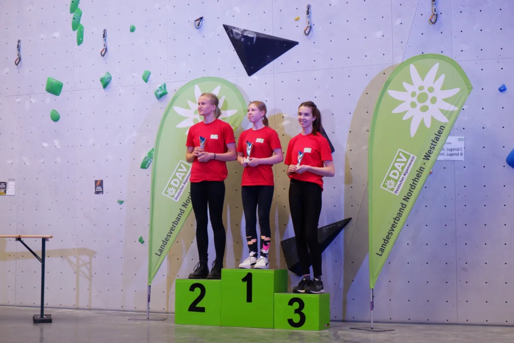 Drei Mädchen in roten Shirts stehen auf dem Siegerpodest vor DAV-Bannern. | © DAV Dortmund