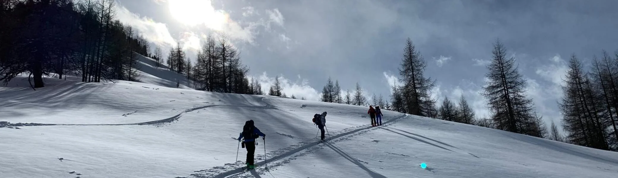 Eine Skitourengruppe zieht Spuren durch glitzernden Schnee bei tief stehender Sonne und leicht bewölktem Himmel. | © DAV Dortmund
