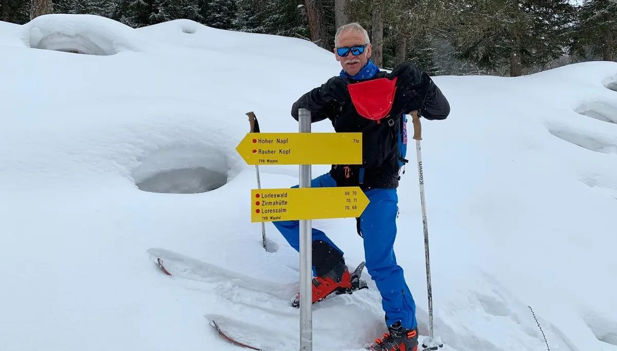 Ein Mann mit Tourenski steht an einem gelben Wegweiser im verschneiten Wald. | © DAV Dortmund