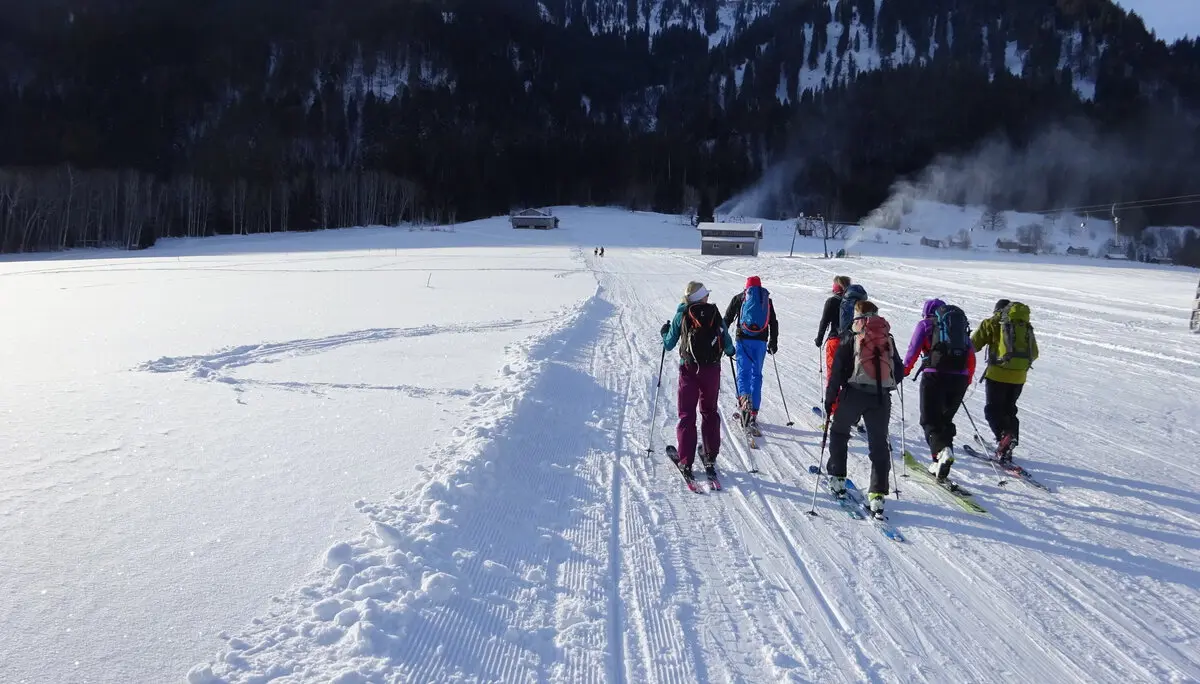 Eine Gruppe Skitourengeher*innen startet auf einer flachen Schneefläche Richtung Wald und Berge. | © DAV Dortmund