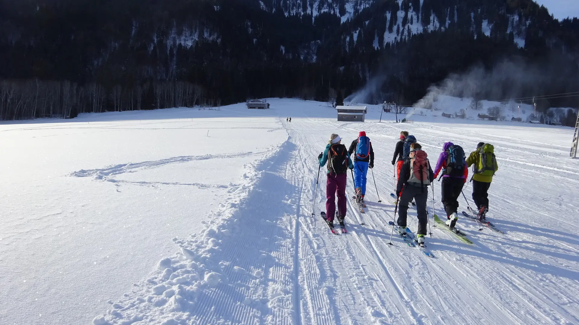 Eine Gruppe Skitourengeher*innen startet auf einer flachen Schneefläche Richtung Wald und Berge. | © DAV Dortmund