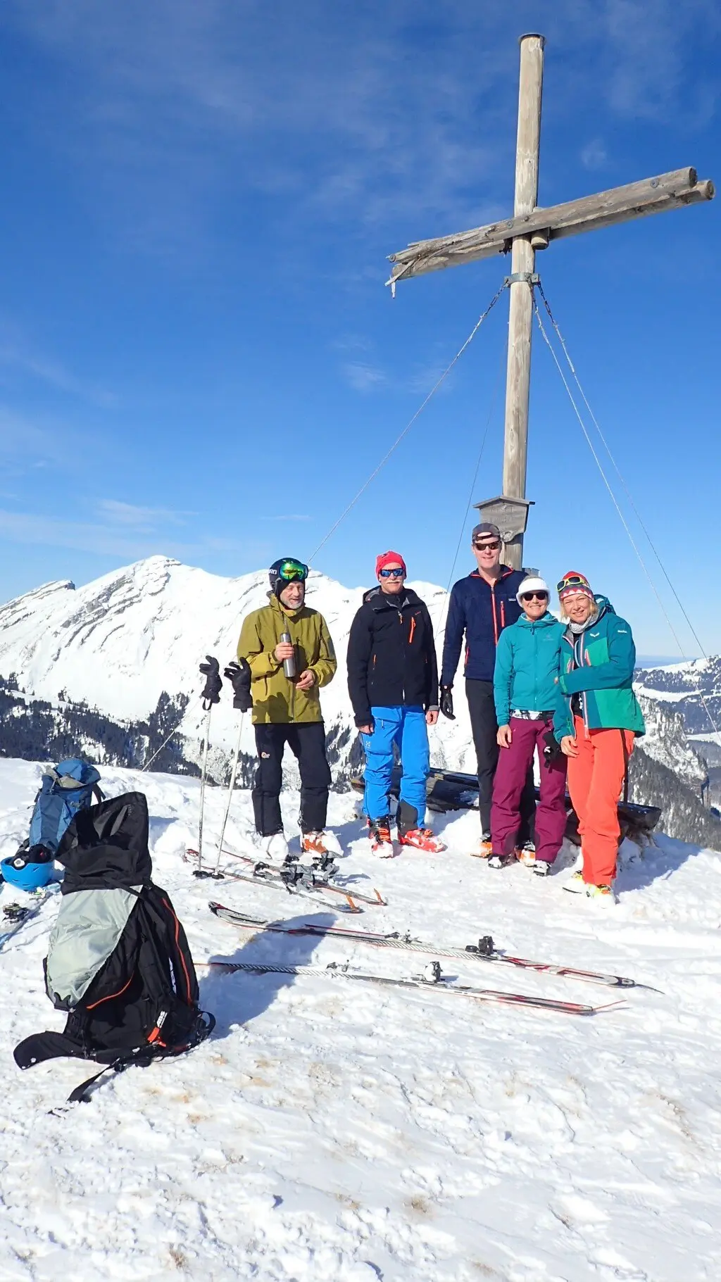 Fünf Personen stehen bei Sonnenschein mit Tourenski am Gipfelkreuz, Rucksäcke und Skier liegen im Schnee. | © DAV Dortmund