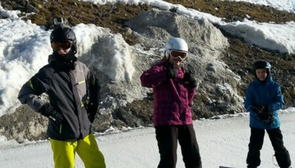Drei Personen stehen mit Snowboards nebeneinander auf einer Piste vor schneebedecktem Hang. | © DAV Dortmund