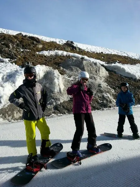Drei Personen stehen mit Snowboards nebeneinander auf einer Piste vor schneebedecktem Hang. | © DAV Dortmund