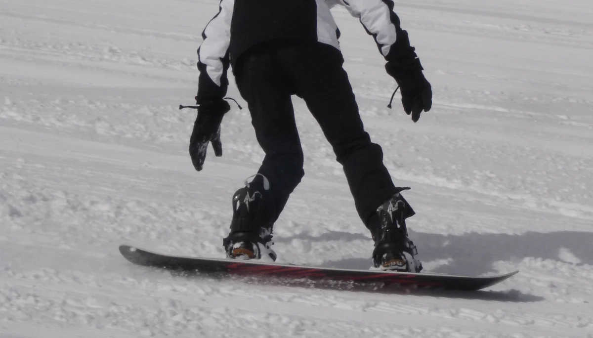 Eine Person fährt mit dem Snowboard auf einer präparierten Piste, Rückenansicht. | © DAV Dortmund