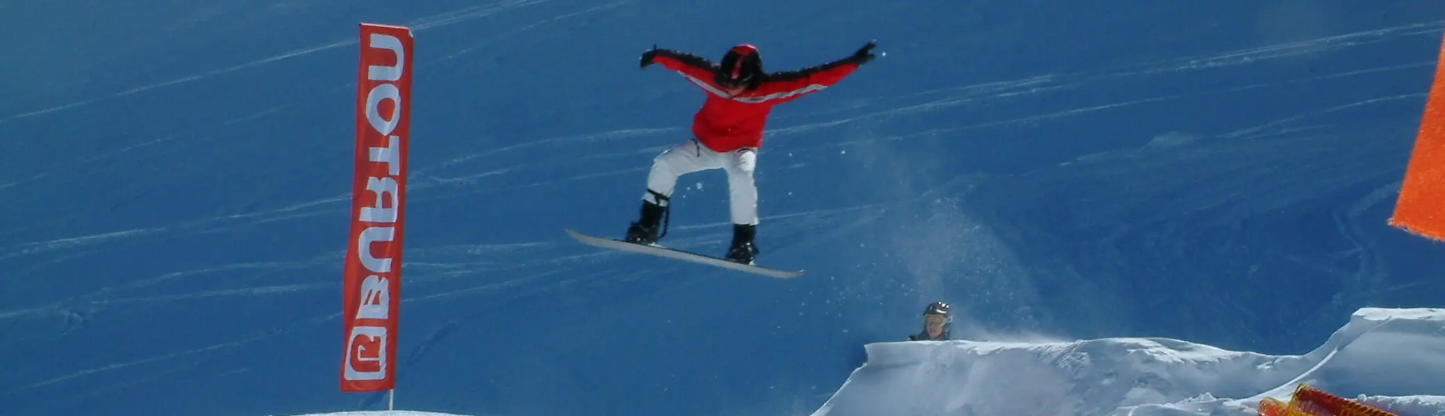 Eine Person springt mit einem Snowboard über eine Rampe im Schneepark, im Hintergrund ein Banner mit „Burton“. | © DAV Dortmund