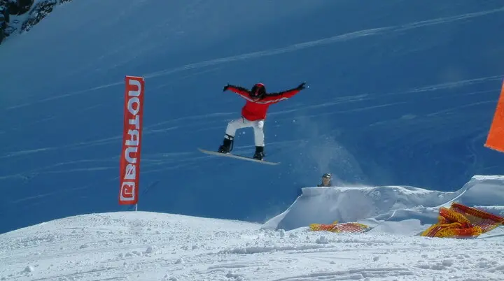Eine Person springt mit einem Snowboard über eine Rampe im Schneepark, im Hintergrund ein Banner mit „Burton“. | © DAV Dortmund