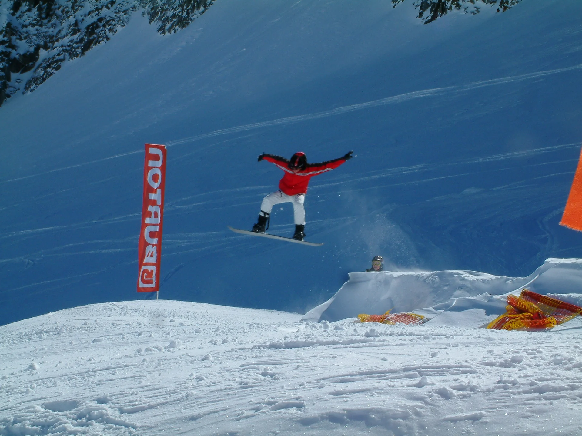 Eine Person springt mit einem Snowboard über eine Rampe im Schneepark, im Hintergrund ein Banner mit „Burton“. | © DAV Dortmund