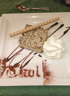 Ein dekorativ angerichtetes Dessert mit Sahne, Eiswaffel und Schokoschrift „Tirol“ auf einem Teller. | © DAV Dortmund