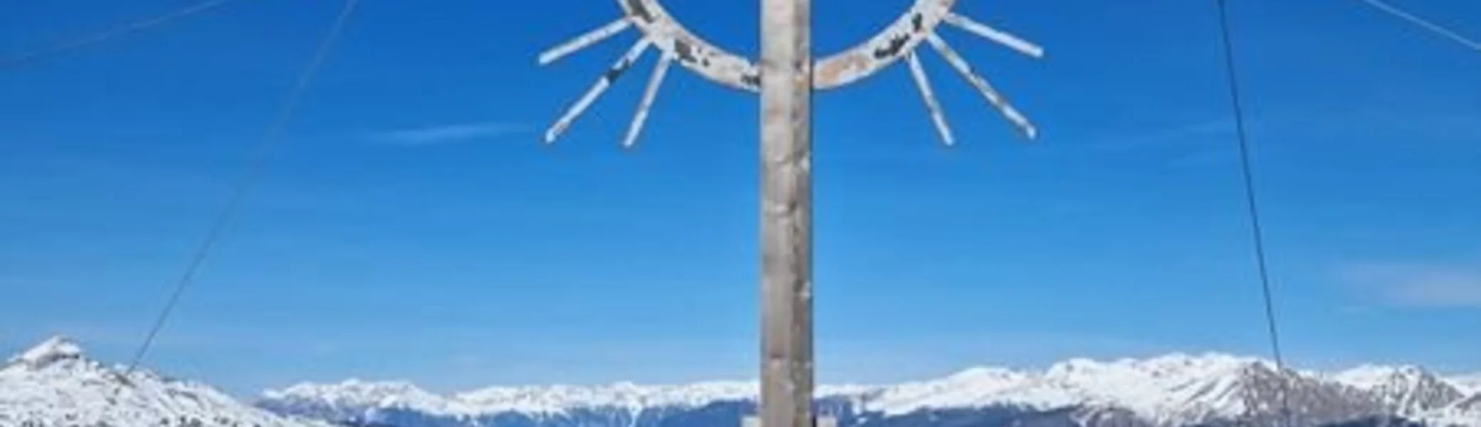 Eine Skitourengruppe steht unter einem Gipfelkreuz mit Strahlen in einer verschneiten Alpenlandschaft. | © DAV Dortmund