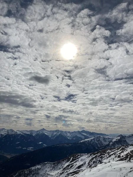Die Sonne scheint durch dramatische Wolken über einer verschneiten Gebirgskette. | © DAV Dortmund