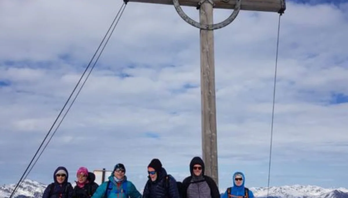 Sieben Personen stehen mit Tourenski unter einem großen Gipfelkreuz auf einem verschneiten Berggipfel. | © DAV Dortmund