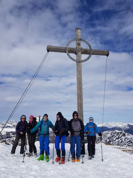 Sieben Personen stehen mit Tourenski unter einem großen Gipfelkreuz auf einem verschneiten Berggipfel. | © DAV Dortmund