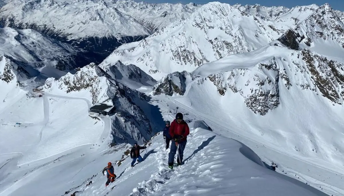 Gruppe auf Skitour steigt einen verschneiten Bergkamm mit Panorama auf die umliegenden Alpen hinauf. | © DAV Dortmund